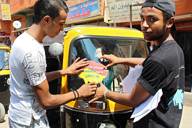 Volunteers affix a sign to tuktuk reading:  My Tuktuk is safe; free from sexual harassment or drugs. Photo: CARE/Salma Salim